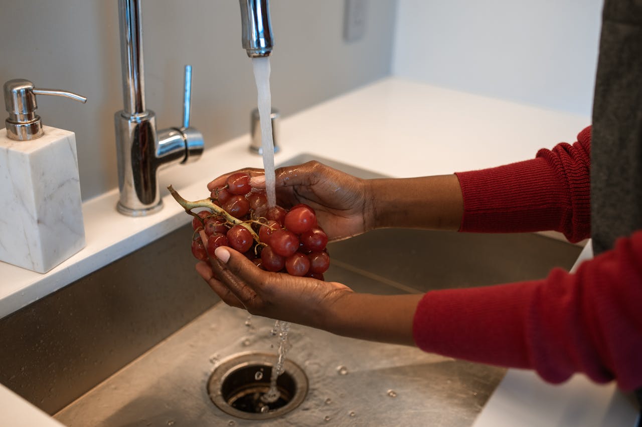 Fresh red grapes being washed in a kitchen sink, emphasizing clean eating and hygiene.
